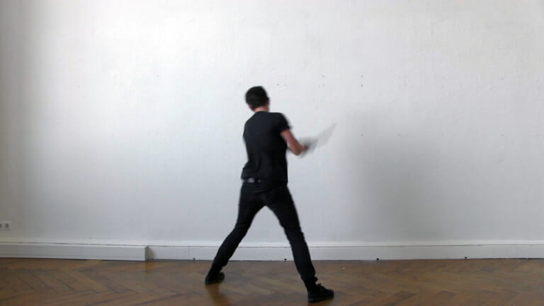 The scenario repeats itself. The person has now placed one foot further towards the wall and seems to lunge from the right to strike. The stick can now be seen blurred and moving at chest level.