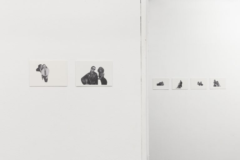 View of a corner of the room with white walls. Across the corner, in A5 landscape format, six white sheets hang on the wall with cut-out figures on them. They are printed in black and white. Most of them are in pairs each, some in tender or erotic poses. By the clothes it is recognizable that they must be historical photographs of different times, for example, the 1920s and 1980s.