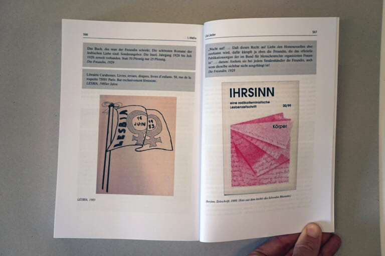 Opened double page, held by a hand on the right. On both sides gray boxes with text, on the bottom left a picture of a drawn flag that reads "LESBIA, June 1983" and the symbol of lesbians. On the bottom right an image of a cover that reads "IHRSINN, a radical feminist lesbian magazine."